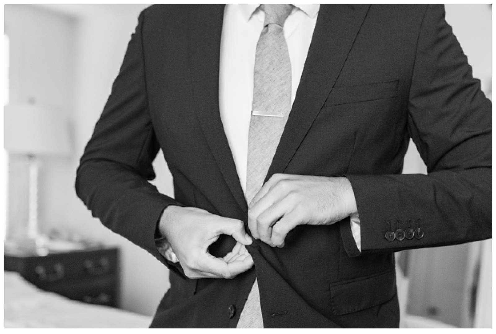 black and white of groom buttoning up jacket