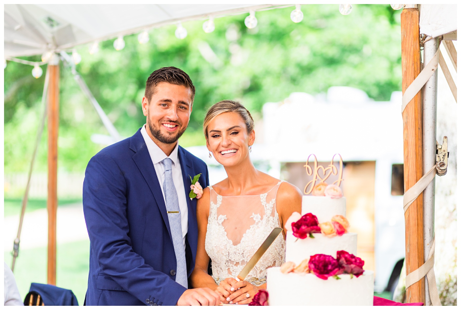 bride and groom standing behind cake smiling